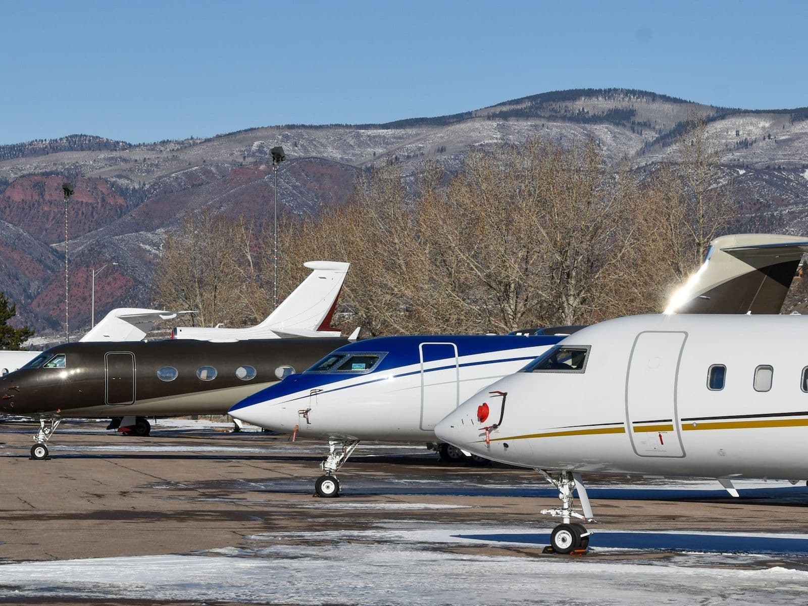Private jets of different makes and operators parked side by side, mountains behind.