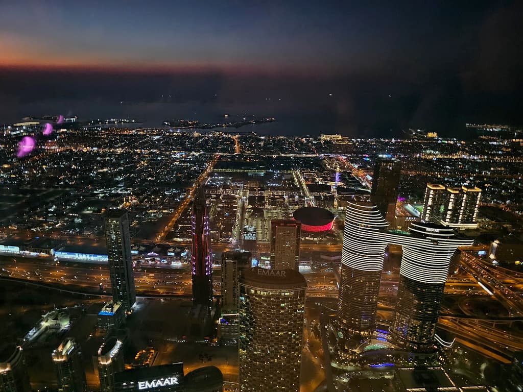 Dubai at night, seen from above, lit towers running out to the coast.