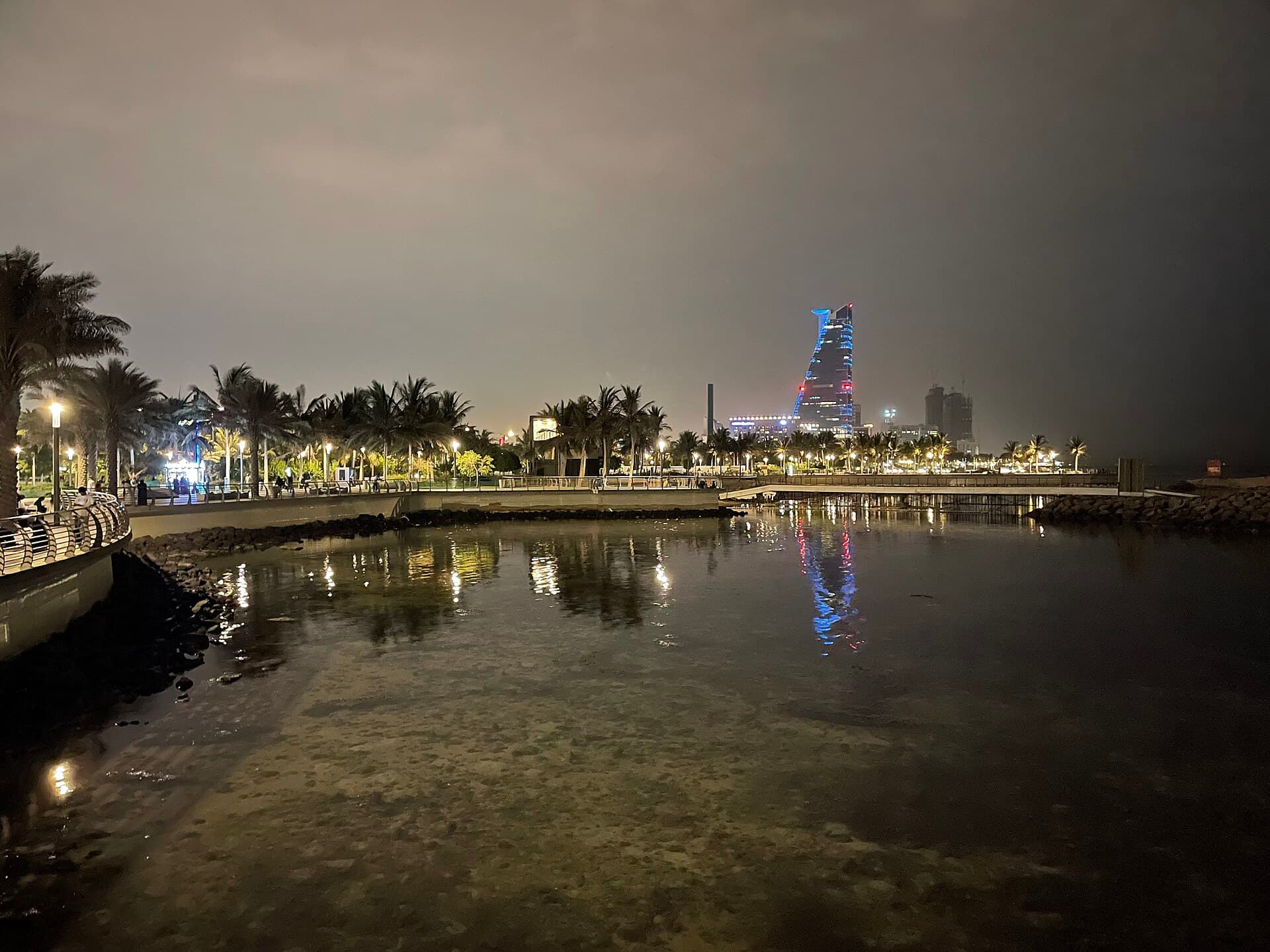 The Jeddah Corniche at night, palms and tower lights reflected in the water.